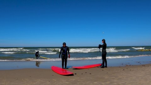 Kaliningrad, Russia, 12, March, 2022:
Two girls in diving suits on the seashore after surfing in the cold Baltic Sea, two girls on the shore of the cold sea