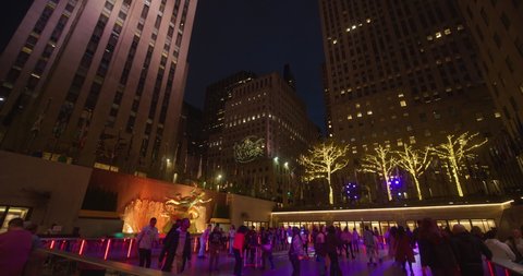 New York, New York United States - April 23,  2022: Pan down from top of 30 Rockefeller Center to Flippers Roller Boogie Palace at the Rink in Rockefeller Center. Nighttime under the lights.