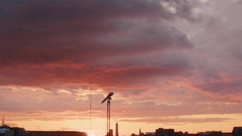 Time lapse of incredible colorful sky clouds at sunset golden hour going from rich yellow orange to dark heavy grey and black. Crane and city skyline low in frame. Dramatic cinematic time lapse.