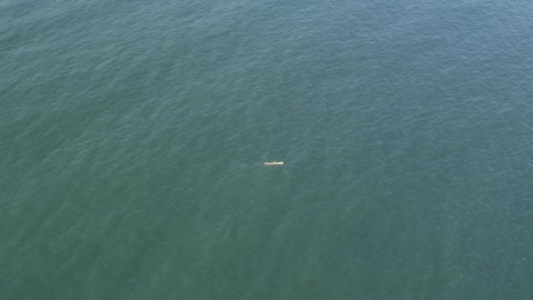 Aerial: Sea kayaker paddles hard L to R, isolated on vast green ocean