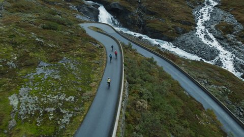 Professional road cyclist on fast and light carbon bicycle descends mountain serpentine road in Norway. Fit, athletic team, friends group on recreational ride trip, training camp, enjoy time outdoors
