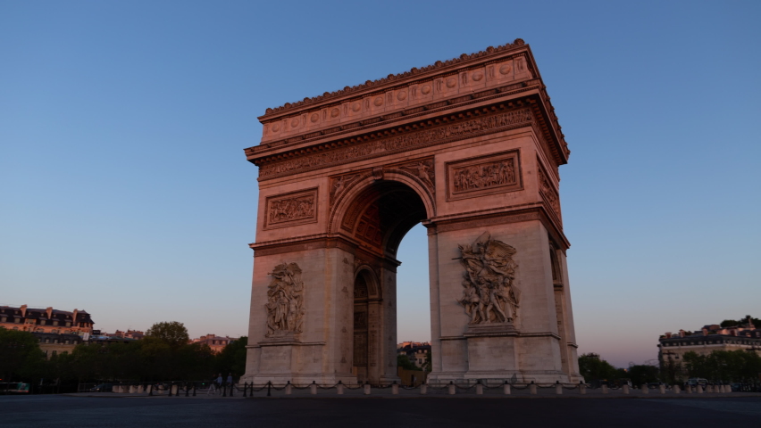 Paris France: Triumphal Arch of the Star (Arc de Triomphe de l'Étoile) - a famous landmark and tourist attraction at sunrise. Traffic on the street on a sunny morning under clear blue sky - hyper-lapse. Royalty-Free Stock Footage #1089722549