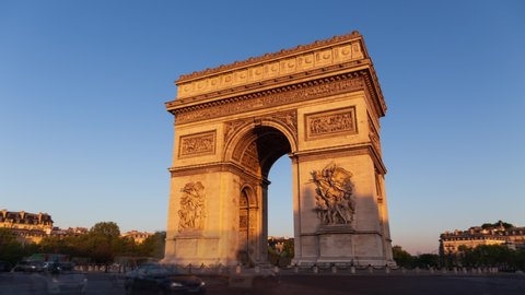 Paris France: Triumphal Arch of the Star (Arc de Triomphe de l'Étoile) - famous landmark and tourist attraction at sunrise. Traffic on the street on a sunny morning under clear blue sky - hyper-lapse.