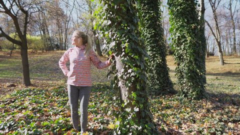 The girl admires the ivy-covered tree and the nature all around.