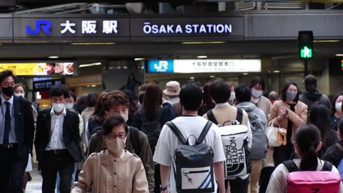 OSAKA, JAPAN - APRIL 2021 : Crowd of people wearing surgical masks to protect from Coronavirus (COVID-19) at the street around Osaka train station. Slow motion shot.