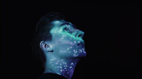 Close Up Shot of a Caucasian Man Face on a Black Background As Colourful Light Projects On His Face, Looking Around in Awe.