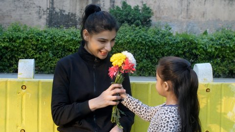 A little adorable schoolgirl brings a bouquet of colorful flowers for her mother - mother's day celebration, and parent-child bonding. A pretty female hugging and cuddling with her little daughter.