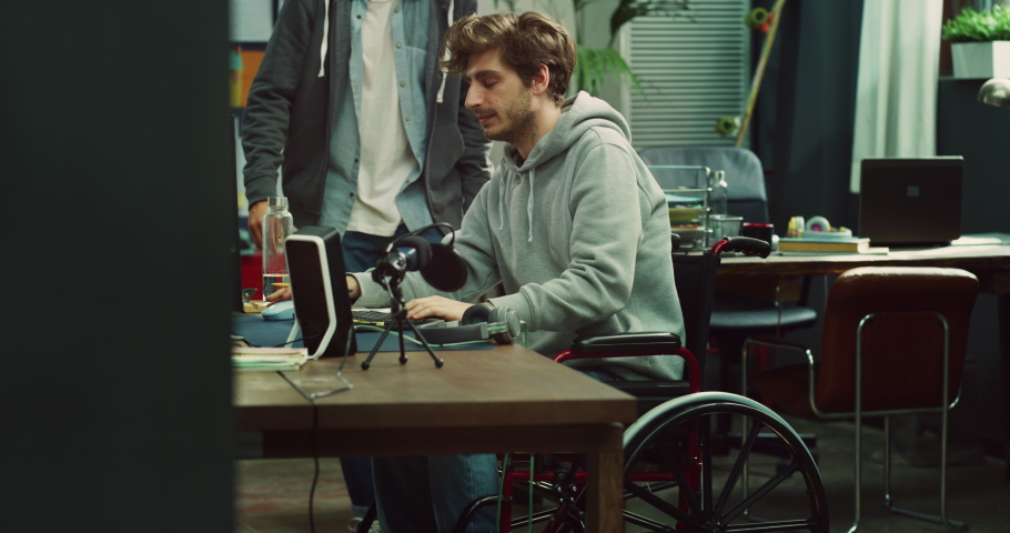 Cinematic shot of young male graphic designer with disabilities use wheelchair and his colleague are discussing about new strategy while working together on project in modern creative studio. Royalty-Free Stock Footage #1089726717