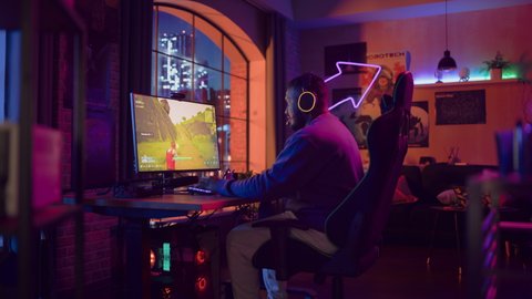 Excited Gamer Playing PvP Shooter Video Game in Which Players Fight in a Battle Royale Tournament on His Personal Computer. Room and PC with Neon Lights. Stylish Black Man in Cozy Room at Home.
