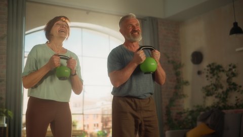 Happy Middle Aged Couple Doing Morning Exercises and Kettlebell Workout Together at Home in Sunny Living Room. Concept of Healthy Lifestyle, Fitness, Recreation, Couple Goals and Retirement.