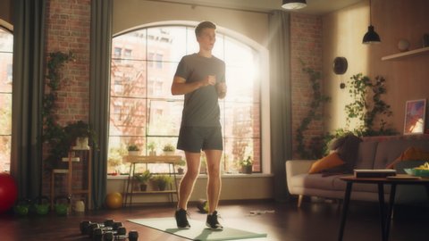 Strong Athletic Fit Young Man Doing Cardio High Knees and Core Strengthening Exercises During Morning Workout at Home in Sunny Apartment. Fitness and Recreation Concept.