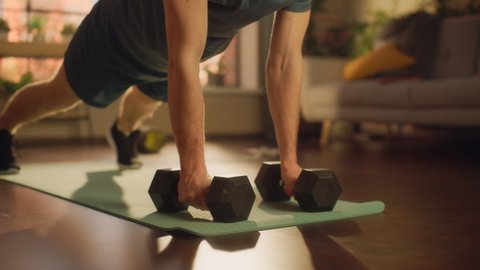 Masculine Athletic Fit Young Man Performing Enduring Training in Plank Position, while Lifting Dumbbells During Morning Workout at Home in Sunny Apartment. Concept of Healthy Lifestyle and Fitness.