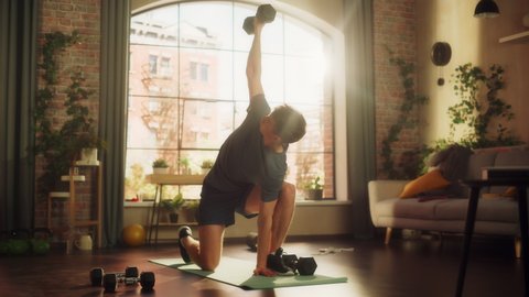 Fit Athletic Strong Young Man Training and Strengthening Arm Muscles with Dumbbell Exercises During Morning Workout at Home in Sunny Apartment. Concept of Healthy Lifestyle and Fitness.