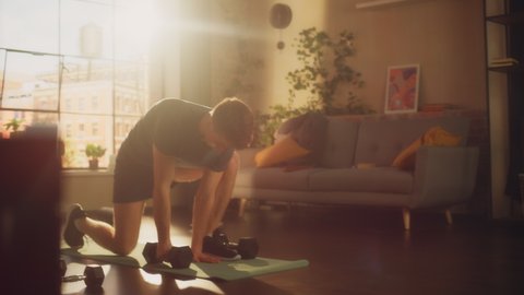 Strong Athletic Fit Young Man Doing Core Strengthening Exercises with Dumbbells During Morning Workout at Home in Sunny Apartment. Concept of Healthy Lifestyle and Fitness.