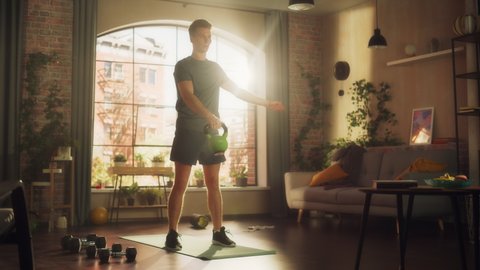 Strong Athletic Fit Young Man Swinging a Heavy Kettlebell from Hand to Hand, Doing Core Strengthening Exercises During Morning Workout at Home in Sunny Apartment. Concept of Health and Fitness.
