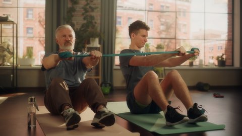 Middle Aged Man Exercising at Home with Personal Trainer. Senior Male Strengthening Core Muscles with Elastic Rope Workout. Young Man Supporting and Guiding Him Through the Training.