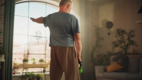 Senior Man Feeling Uncomfortable Sudden Back Pain During Morning Workout, While Exercising with Heavy Kettlebell at Home. Middle Aged Male Grabbing His Back to Ease the Pain.