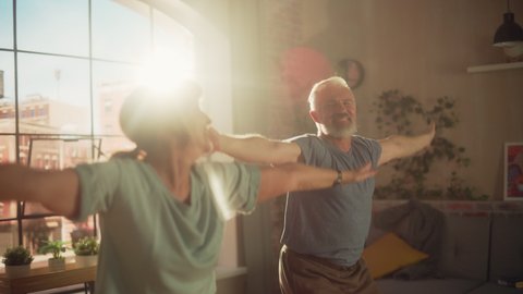 Happy Smiling Senior Couple Doing Gymnastics and Jumping Jacks Exercises Together at Home on Sunny Morning. Concept of Healthy Lifestyle, Fitness, Recreation, Couple Goals, Wellbeing and Retirement.