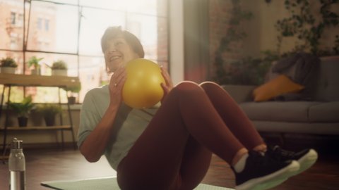 Portrait of a Senior Woman Exercising and Training at Home on Sunny Morning. Elderly Female Doing Crunches, Stretching Arms, Body and Muscles in Loft Apartment Living Room for Wellness and Fitness.