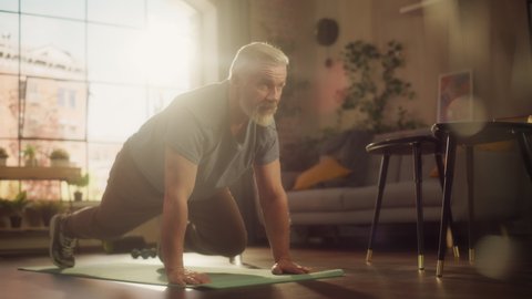 Strong Athletic Fit Middle Aged Man Doing Mountain Climber Exercises During Morning Workout at Home in Sunny Apartment. Concept of Healthy Lifestyle, Fitness, Recreation, Wellbeing and Retirement.