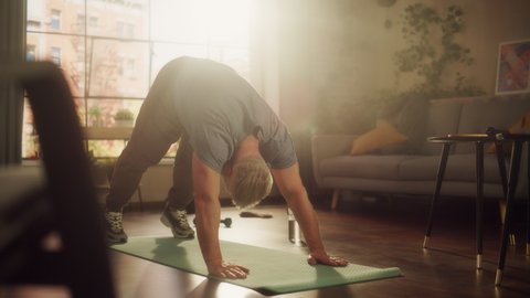 Strong Athletic Fit Senior Man Training on a Yoga Mat, Doing Back Stretching and Core Strengthening Exercises During Morning Workout at Home in Sunny Apartment. Concept of Health and Fitness.