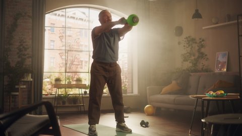 Strong Athletic Fit Middle Aged Man Lifting and Swinging a Heavy Kettlebell, Doing Core Strengthening Exercises During Morning Workout at Home in Sunny Apartment. Concept of Fitness Lifestyle.