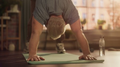 Portrait of a Strong Fit Senior Man Training on a Yoga Mat, Doing Back Stretching and Core Strengthening Exercises During Morning Workout at Home in Sunny Apartment. Concept of Health and Fitness.