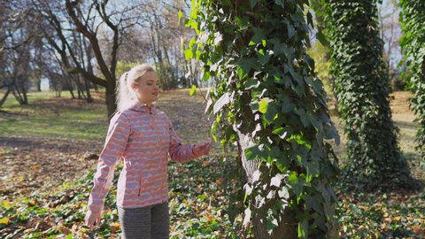 A girl walks around an ivy-covered tree.