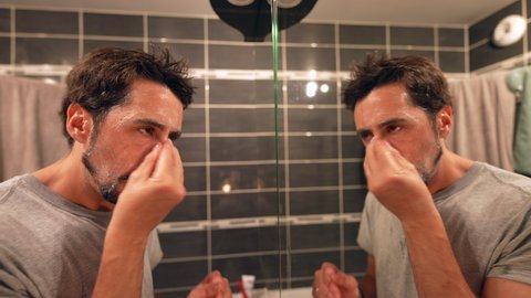 Person washing face in front of bathroom mirror man using facial cleanser at night routine