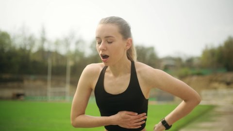 Attractive young woman feeling chest pain during morning jogging on the stadium. Heart attack while run. Health care.