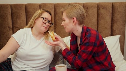 two beautiful women. lgbt couple, one woman plus size, have breakfast in bed, one feeds the other and they kiss. romantic breakfast. love relationship, happiness