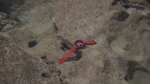 May 20, 2021 Cyprus, pathos. Tourist sports watch Garmin INSTINCT Flame Red in water on stone. Man takes protected watch with gps navigation from transparent sea water for travel and exploration.