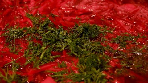 Cooking at home. Macro shot of the surface of borscht in a saucepan, sprinkled with fresh dill. Hot red beetroot soup is stirred with a ladle, the pan is covered with a lid.