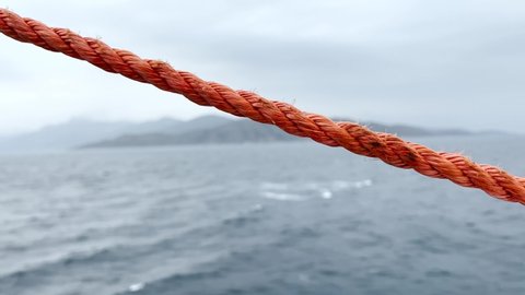 Shrouds and ropes of an old sailboat in the open sea. orange rope closeup in front of open blue sea. grey night in the open ocean