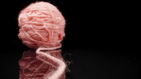 A ball of pink woolen threads, on black glass.. Dolly slider extreme close-up. Laowa Probe