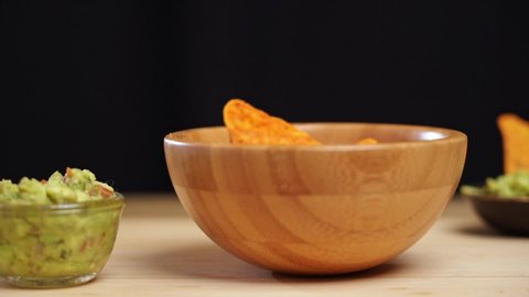 Slow Motion shot of tortillas chips falling in plate. Falling nachos in wooden bowl. Traditional Mexican food. nachos served with guacamole is Avocado, tomato  and cilantro. cheese Potato Chips.