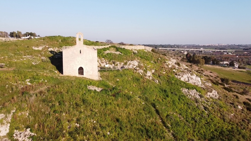 Aerial shot from a drone of a green hilly landscape on the top of which there is an ancient medieval church
