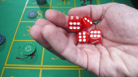 Male hand shakes red dice in slow motion against the background of a green roulette table in a casino. Man gambler, gambling, craps, poker. Casino chips are laid out on the gaming table close up.