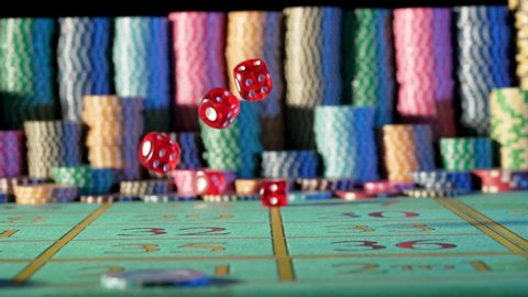 Red dice falling on a gaming table in a casino on a black background with blurry chips. Craps, poker, blackjack. Concept of betting, entertainment, leisure. Close up in slow motion.