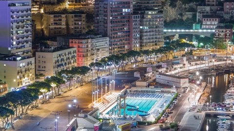 Seaside swimming pool in Monaco night timelapse, buildings in the background. Aerial top view. Traffic on the road of embankment