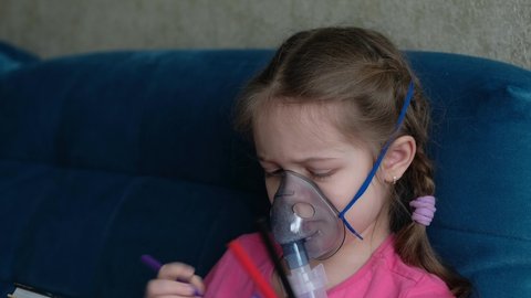 Little girl makes an inhalation vapor and draws a drawing. Child is sick and breathes through an inhaler in home. 