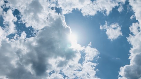 Low angle timelapse bright sun on blue summer sky with moving fluffy clouds, sun shining sunbeams, white cumulus clouds on sunshine day. Time-lapse, sun rays daylight, sunny cloudscape