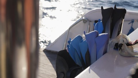 Stack of flippers and diving masks on board of ship sailing in the sea, sunshine reflecting in water overboard. Gear for scuba diving, underwater adventure, extreme sports