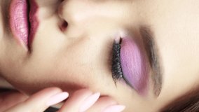 Closeup slow motion vertical video of human female face. Footage of woman with hand near face and nails with pink manicure. Green eyes are with pink shadows beauty makeup.