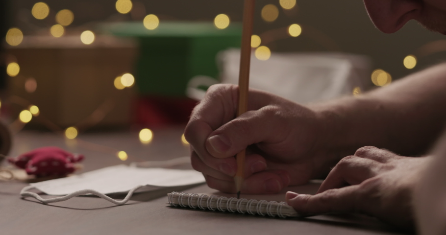 Slow motion closeup man writes Shopping list in notepad with a pencil under warm light in the evening with medicine mask near hand