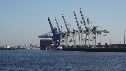 HAMBURG, GERMANY - MARCH 19, 2022: Container Terminal with Ships being loaded in the busy Port of Hamburg in sun. Slow Motion, Slo-Mo. Containers being moved around behind the large Container Cranes.