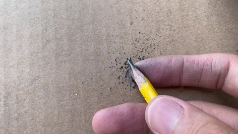 Male hand artist sharpening pencil with a sharp silver blade knife close up shot, educational and carpentry concept with cardboard box background - day