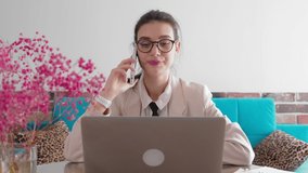 A young business woman is sitting in a home office, typing on a wireless laptop and talking on the phone. Remote work at home.