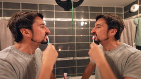 Person brushing teeth in front of bathroom mirror at night routine
