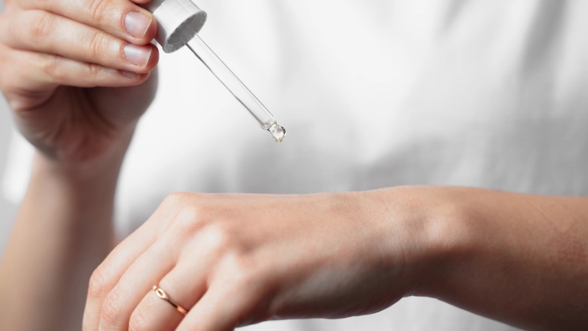 Close up of white woman hand applying oil of essential oil or serum for skin. Self care concept 